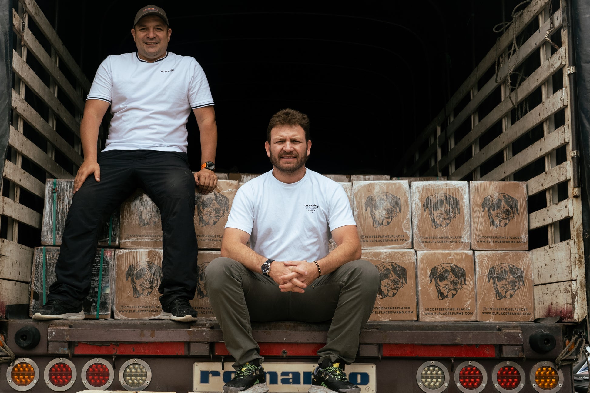 Sebastian Ramírez with a friend sitting on a truck packed with boxes of fresh coffee ready to be shipped.