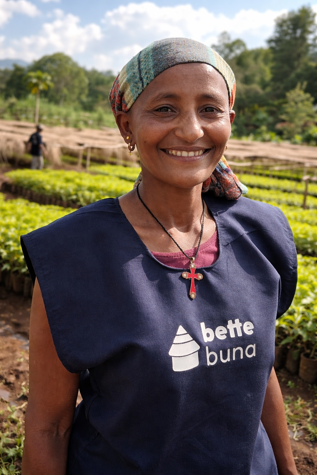 Female coffee producer standing in a coffee nursery at Bette Buna with young plants and drying beds in the background