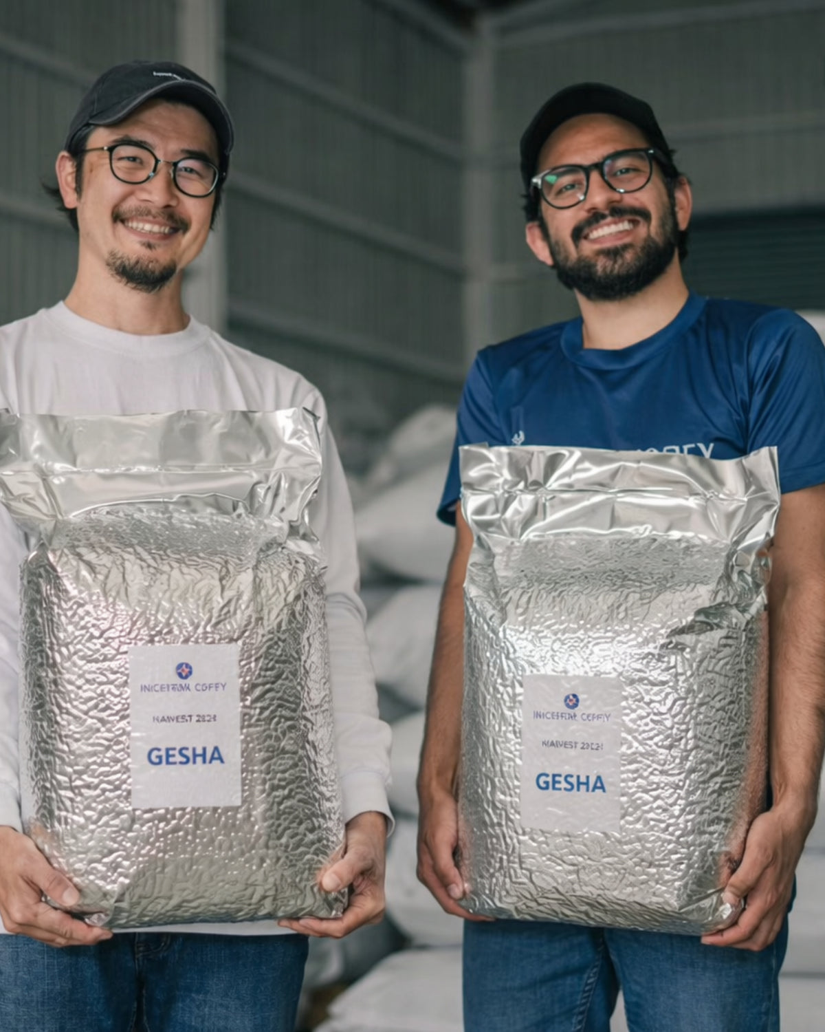 Two men holding large bags of Gesha coffee beans in a warehouse setting.