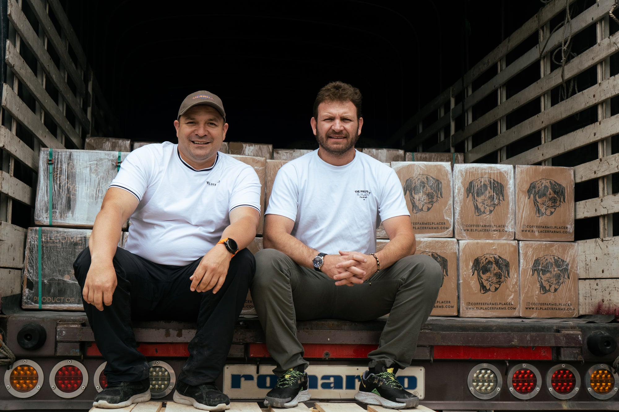 Sebastian Ramírez and friend sitting on a truck bed with stacked fresh coffee boxes ready to be shipped