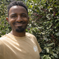 Dawit Syoum standing in a coffee plot at Bette Buna with ripe cherries visible on the plants behind him